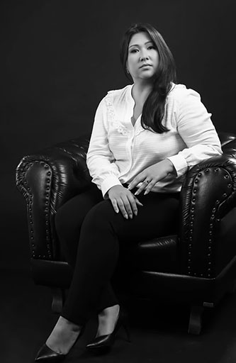 foto preto e branco de Priscilla Michiko com uma camisa branca, calças pretas, sentada numa poltrona de couro preta